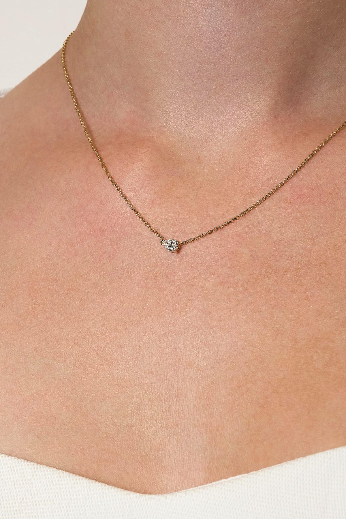 Necklace with a lab grown diamond pendant on a person's neck against a neutral background