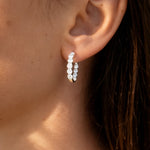 Lady's ear wearing a pair of white gold hoop earrings with clear lab grown diamonds on a white background
