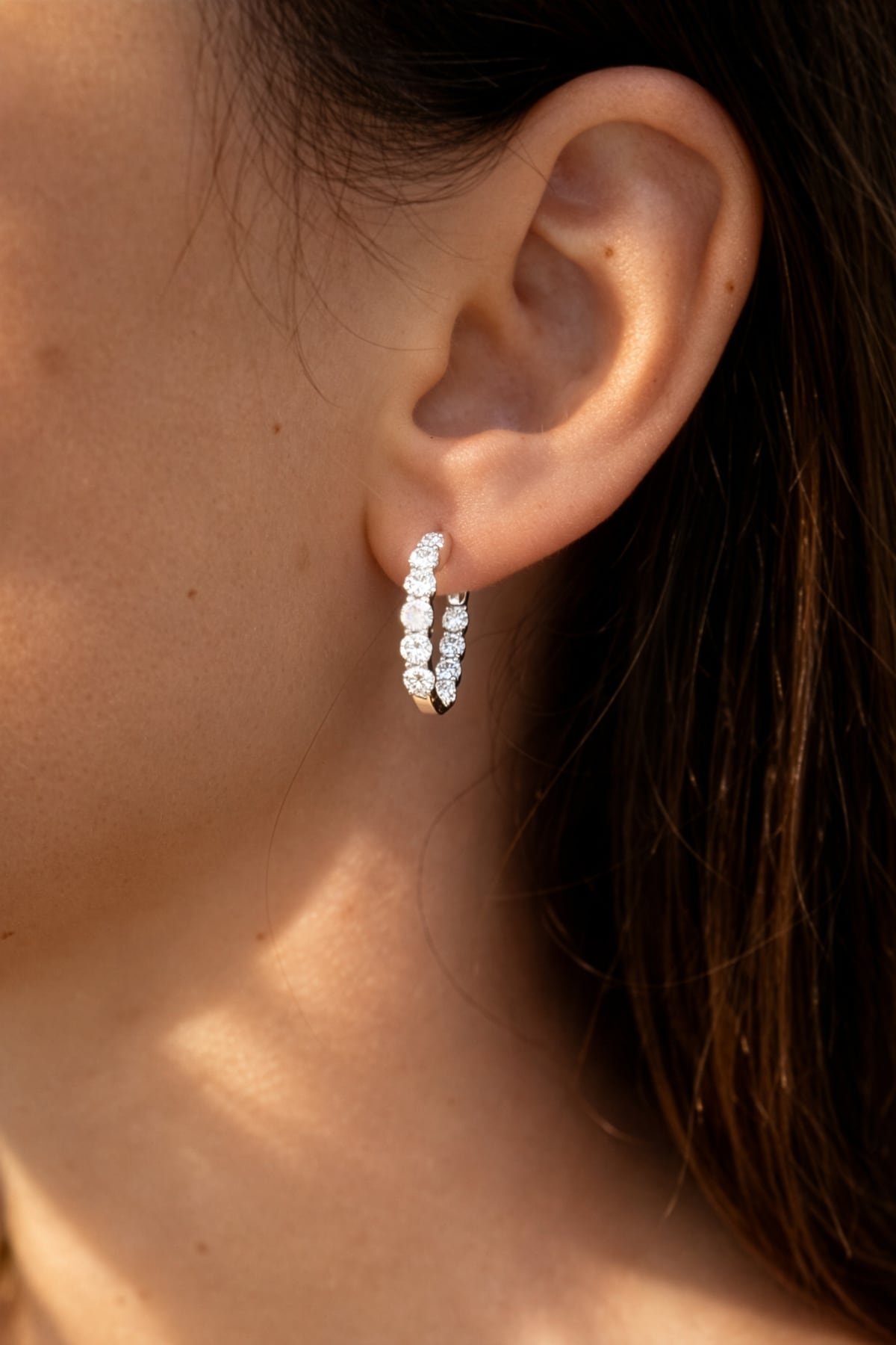 Lady's ear wearing a pair of white gold hoop earrings with clear lab grown diamonds on a white background