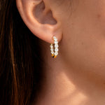 Lady's ear wearing a pair of yellow gold hoop earrings with clear lab grown diamonds on a white background