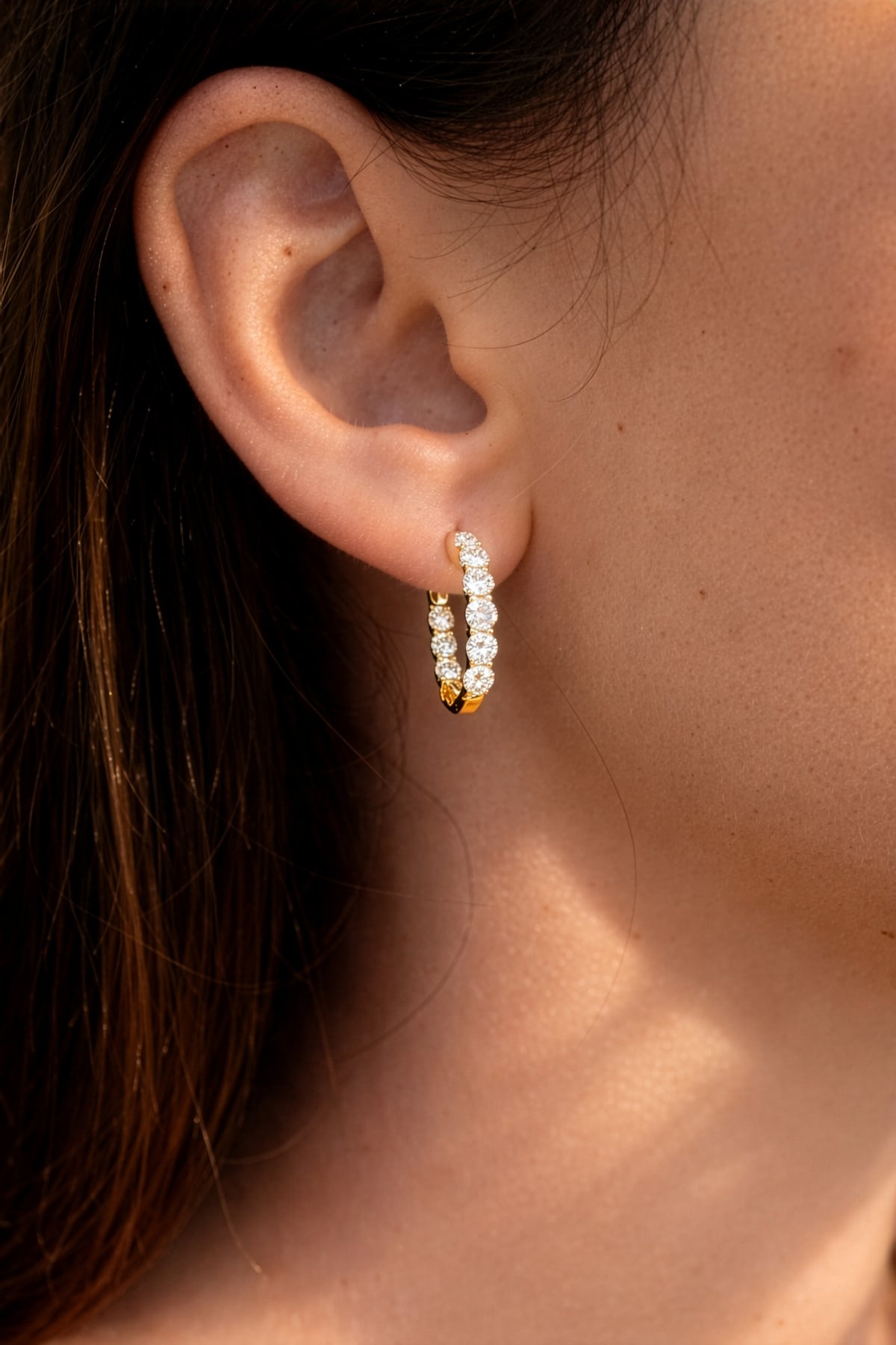 Lady's ear wearing a pair of yellow gold hoop earrings with clear lab grown diamonds on a white background