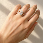 Hand wearing a gold ring with a lab created emerald cut diamond on a beige background