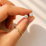 Hand holding a pair of lab diamond stud earrings against a white background