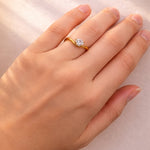 Gold ring with a pear cut lab grown diamond on a hand against a neutral background