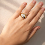 Hand wearing a gold ring with a lab grown diamond on a neutral background