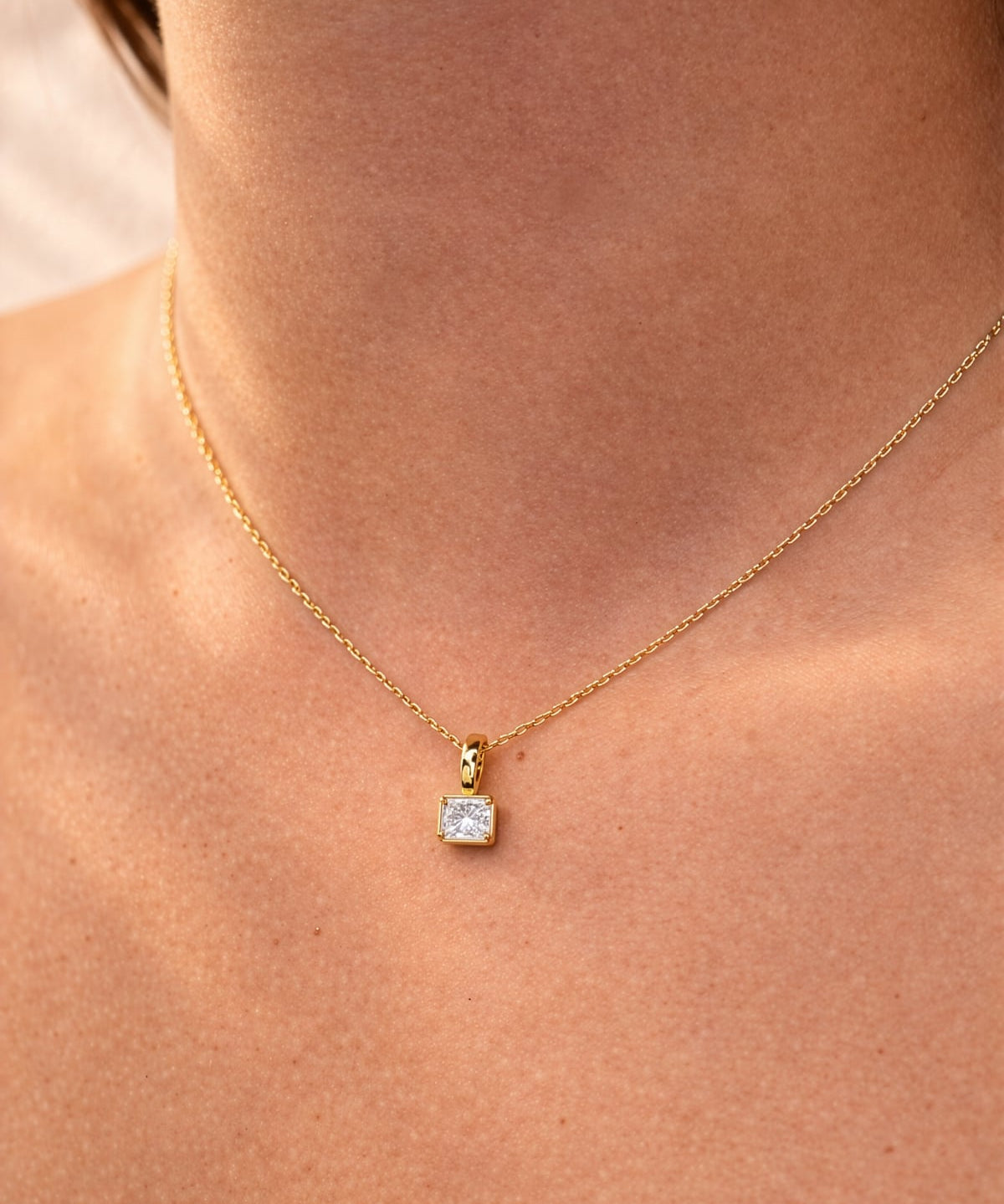 Gold necklace with a square lab grown diamond pendant on a person's neck
