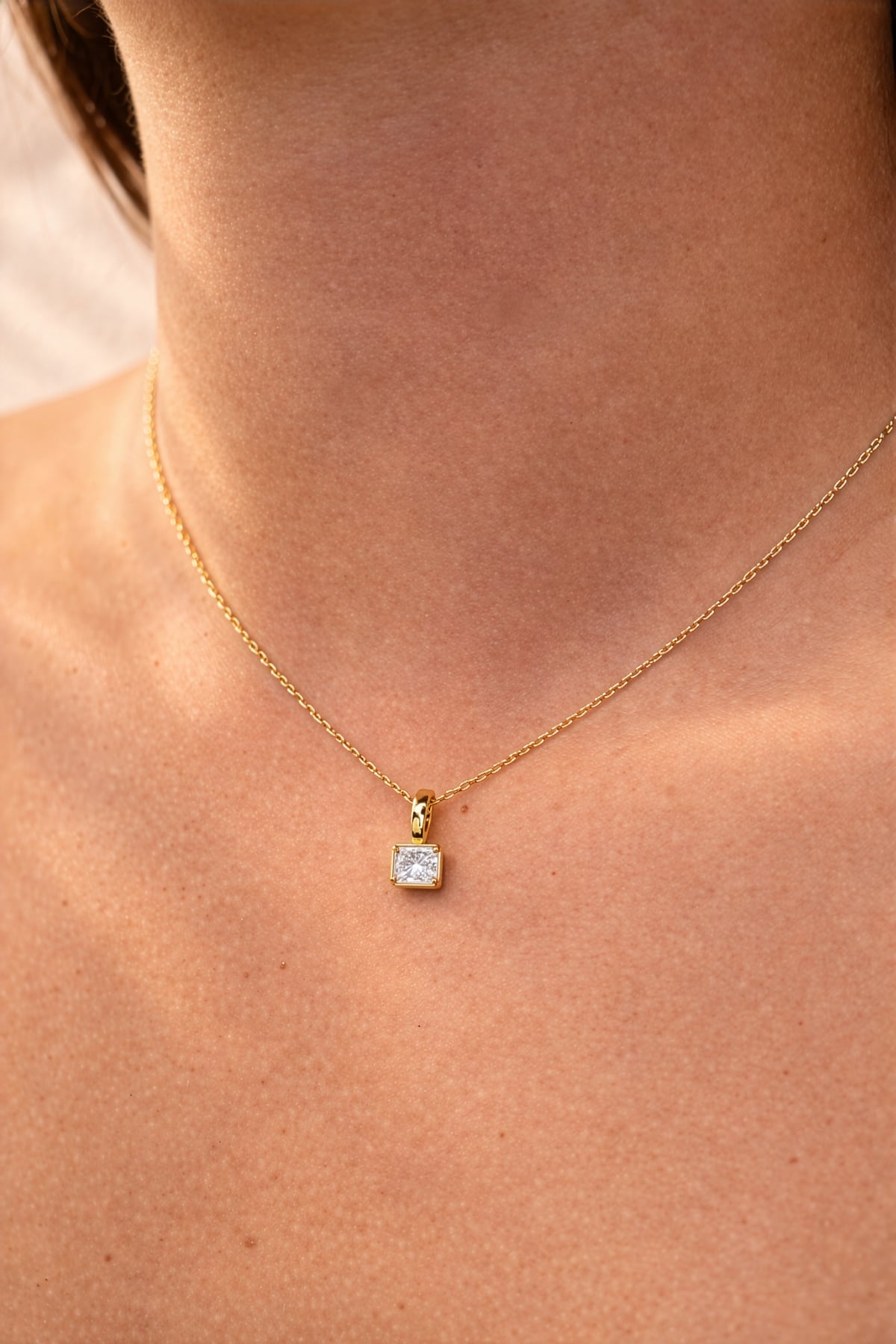 Gold necklace with a square lab grown diamond pendant on a person's neck