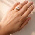 Hand wearing a gold ring with a pear cut lab diamond on a beige background