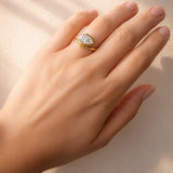 Hand wearing a gold ring with a pear cut lab diamond on a beige background